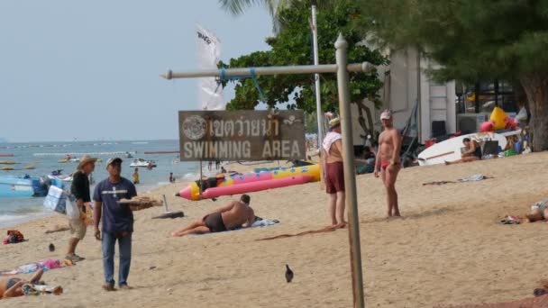 PATTAYA, THAILAND, December 14, 2017: View on the beach promenade with palm trees and coconuts in Thailand. People rest on the beach. A pointer with an inscription in English swimmig area — Stock Video