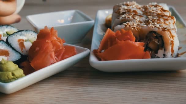 Bonitos e saborosos grandes rolos de sushi branco e preto da cozinha japonesa estão na bandeja na mesa do restaurante. Molho de soja é derramado em um pires — Vídeo de Stock