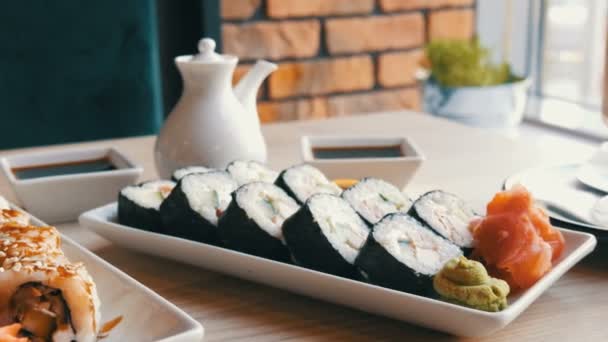 Dos juegos de rollos de sushi en un elegante café bellamente decorado. Restaurante Cocina japonesa en la mesa junto a la tetera de porcelana de sushi para salsa de soja y platillo — Vídeos de Stock