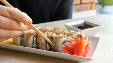 Bir genç çocuk alır suşi rulo Çin bambusu ile sopa ve soya sosu düşerse, bir parça pembe zencefil alır. Yeşil wasabi zencefil ve sosu yanında beyaz porselen tabakta Japon mutfağı