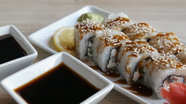 Большие суши из японской кухни лежат на столе в стильном ресторане, рядом с соусом для соевого соуса, васаби, имбиря и ломтика лимона — стоковое видео