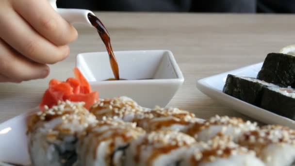 Japanese food. Sushi rolls lie on the table next to ginger wasabi and lemon. Soy sauce is poured from a special porcelain teapot in saucer — Stock Video