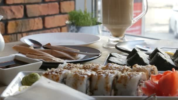 Dos juegos de rollos de sushi en un elegante café bellamente decorado. Restaurante Cocina japonesa en la mesa junto a la tetera de porcelana de sushi para salsa de soja y platillo — Vídeo de stock