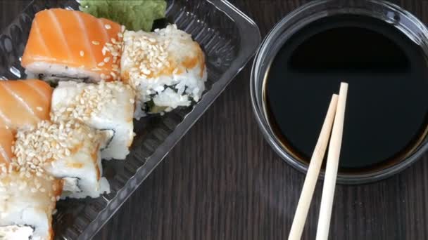Elegantemente establecido sushi conjunto sobre un fondo de madera negro junto a la salsa de soja y palos de bambú chino. Varios rollos de sushi con salmón, anguila, camarones de pepino y otros rellenos diversos — Vídeo de stock