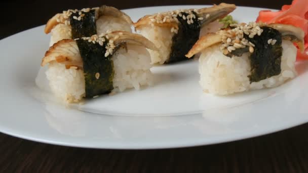 Un grande piatto bianco su cui giacciono quattro enormi sushi con anguille riavvolte con un pezzo di nori accanto allo zenzero rosa e al wasabi verde — Video Stock