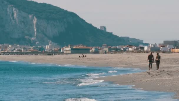 Mladý pár procházky podél pobřeží Středozemního moře na pozadí Rock of Gibraltar, obalená v horké kvasnice vzduchu — Stock video