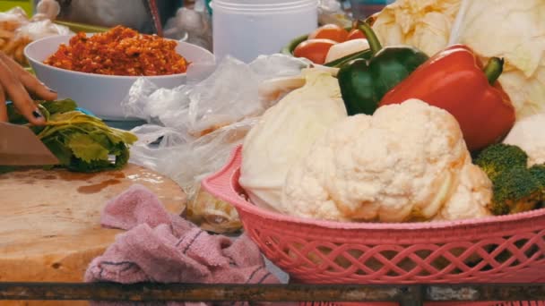 Mulher corta verdes em uma placa de cozinha com uma faca grande vista de perto. Ao lado de legumes e utensílios de cozinha. Thai comida de rua — Vídeo de Stock