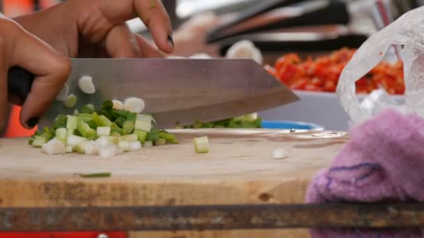 Kobieta kawałki zielonych na boardzie kuchnia z dużym nożem. Obok warzyw i przybory kuchenne. Tajskie street food — Wideo stockowe