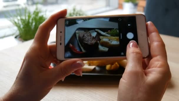 Belas mãos femininas fazem foto de comida de um pedaço de bife suculento em uma placa preta elegante em um smartphone branco — Vídeo de Stock
