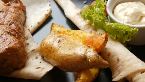 Delizioso pezzo succoso di bistecca di maiale con patate e verdure su un elegante piatto nero nel ristorante — Video Stock
