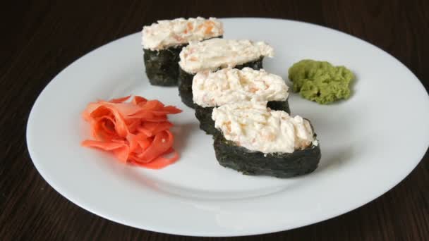 A large white plate on which lies four huge sushi nigiri next to pink ginger and green wasabi — Stock Video