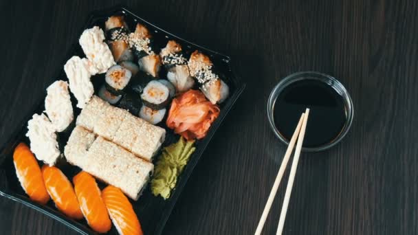 Kamera zoomt. Stilvoll verlegtes Sushi auf schwarzem Holzgrund neben Sojasauce und chinesischen Bambusstäben. verschiedene Sushi-Rollen mit Lachs, Aal, Gurkengarnelen und anderen verschiedenen Füllungen — Stockvideo