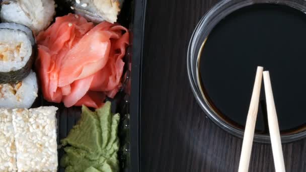 Camera moves up. Stylishly laid sushi set on a black wooden background next to soy sauce and Chinese bamboo sticks. Various sushi rolls with salmon, eel, cucumber shrimps and other various stuffing — Stock Video