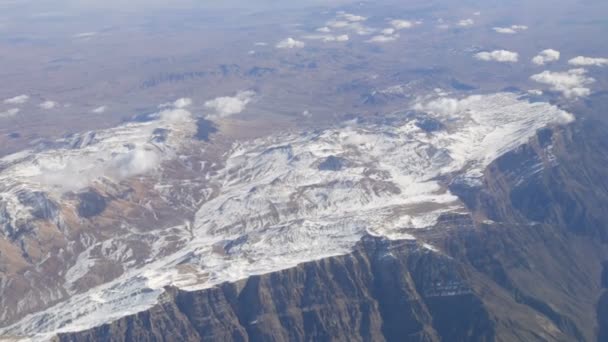 うっすら雪、雲、通り過ぎる飛行機の窓からの眺めと美しい山の範囲 — ストック動画