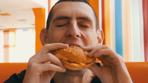 Cute brown-eyed man with an appetite eating big hamburger — Stock Video