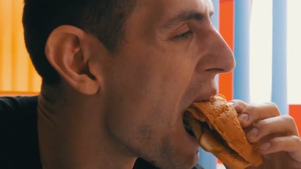 Bonito homem de olhos castanhos com apetite comendo hambúrguer grande — Vídeo de Stock