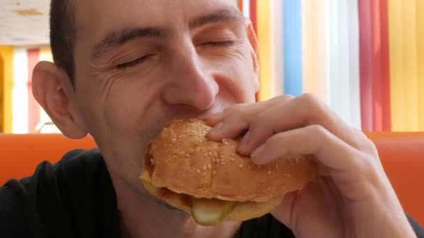 Cute brown-eyed man with an appetite eating big hamburger — Stock Video