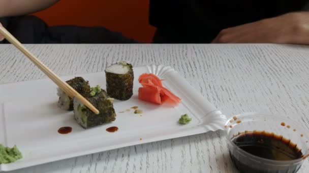El hombre toma un rollo de sushi chino de palillos de bambú y lo sumerge en salsa de soja — Vídeo de stock