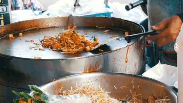 Продавец уличной еды жарит традиционную тайскую рисовую лапшу с яйцами, курицей и капустой. Азиатская еда — стоковое видео