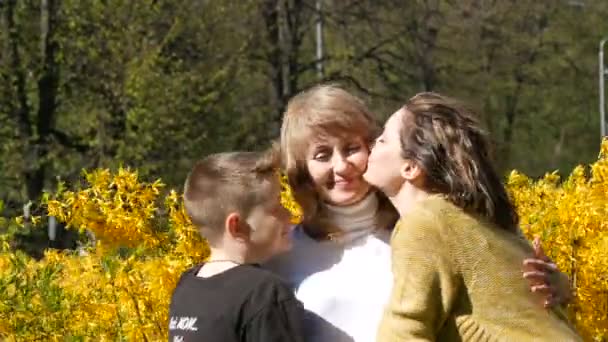 Una figlia adulta e un adolescente incontrano la loro madre anziana abbracciarla e baciarla. Festa delle madri di primavera — Video Stock