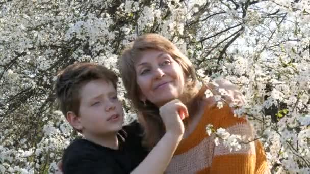 Portrait of an adult middle-aged mother and her teen son who look up at sky against a blossoming tree — Stock Video