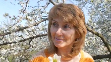 Anneler günü. Mutlu bir şekilde gülümseyerek kameraya bakarak lushly çiçeklenme arka plan üzerinde çiçek kokusu nefes bir güzel mavi gözlü orta yaş kadın portresi ağaç bahar