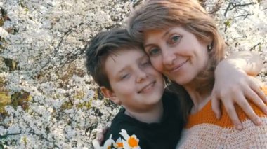 Bir yetişkin orta yaşlı anne hugs ve öper onun gençler şefkatle süslü güzel bir ağaç çerçevede evlat. Anneler günü bahar