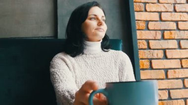Güzel kız ikindilerde içecekler kahve gülümseyen sıcacık bir kafede oturur ve pencereden görünüyor