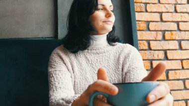 Güzel kız ikindilerde içecekler kahve gülümseyen sıcacık bir kafede oturur ve pencereden görünüyor