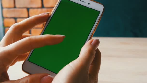 Smartphone de pantalla verde. Tecla de croma en un teléfono inteligente blanco, manos femeninas sostienen el teléfono móvil en un café — Vídeo de stock