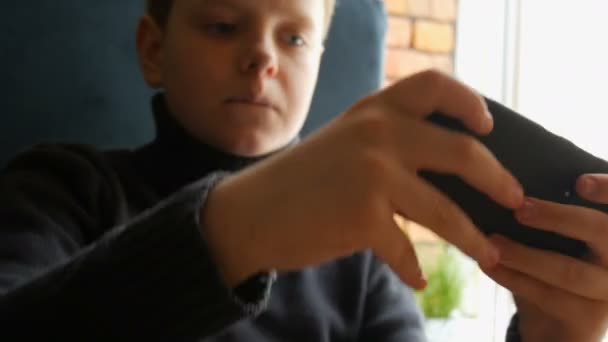 Niño adolescente jugando un juego en el teléfono inteligente negro — Vídeos de Stock