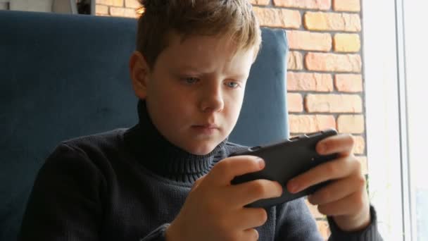 Niño adolescente jugando un juego en el teléfono inteligente negro — Vídeo de stock
