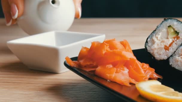 Mãos de mulheres bem tratadas com uma bela manicure despeje molho de soja de um mini bule em panela, ao lado da mesa de sushi — Vídeo de Stock