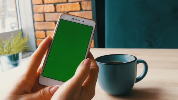 Smartphone cu ecran verde. Chroma Key pe un smartphone alb, mâinile de sex feminin țin telefonul mobil într-o cafenea lângă o ceașcă de cafea — Videoclip de stoc