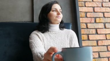 Güzel kız ikindilerde içecekler kahve gülümseyen sıcacık bir kafede oturur ve pencereden görünüyor