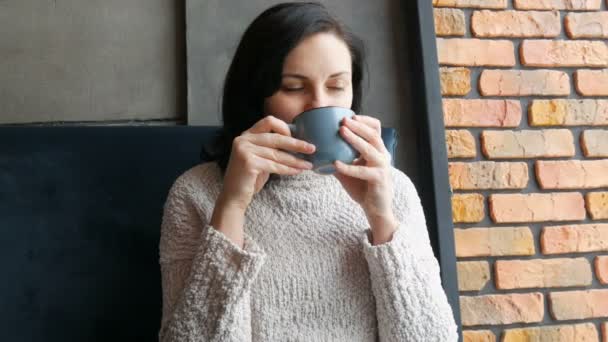 Mooi meisje zit in een gezellig café pensively glimlachend drinken koffie en kijkt uit het raam — Stockvideo