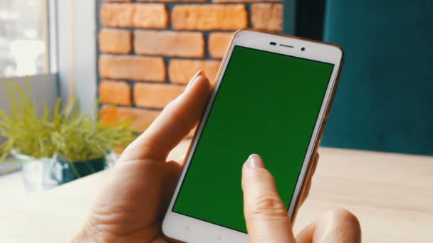 Smartphone de pantalla verde. Tecla de croma en un teléfono inteligente blanco, manos femeninas sostienen el teléfono móvil en un café — Vídeos de Stock