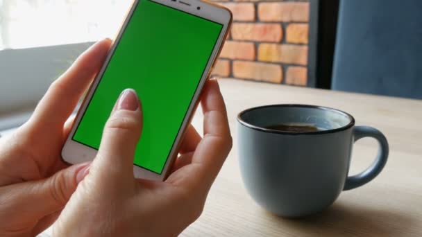 Smartphone cu ecran verde. Chroma Key pe un smartphone alb, mâinile de sex feminin țin telefonul mobil într-o cafenea lângă o ceașcă de cafea — Videoclip de stoc