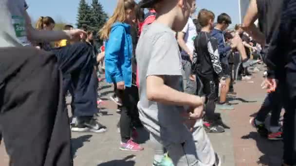 21. April 2018 - Kamenskoje, Ukraine: Viele Menschen machen sich vor dem Marathonlauf warm. Sprünge und Kniebeugen einer großen Anzahl von Menschen auf dem Platz — Stockvideo