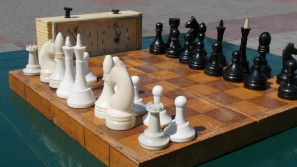 Black and white chess stand on the board, next to a vintage chess clock on street — Stock Video