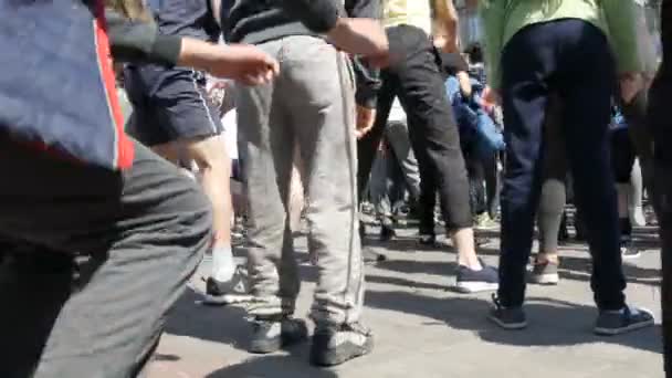 21 aprile 2018 - Kamenskoye, Ucraina: un gran numero di gambe di popoli fanno un riscaldamento prima della gara di maratona. Salti e squat di un gran numero di persone in piazza — Video Stock