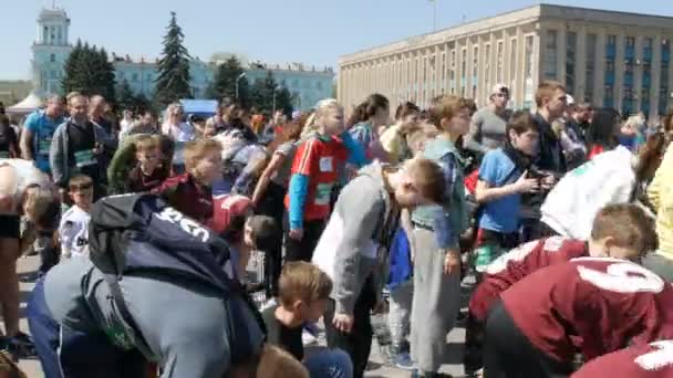 21 de abril de 2018 - Kamenskoye, Ucrania: un gran número de piernas de los pueblos se calientan antes de la carrera maratónica. Saltos y sentadillas de un gran número de personas en la plaza — Vídeos de Stock