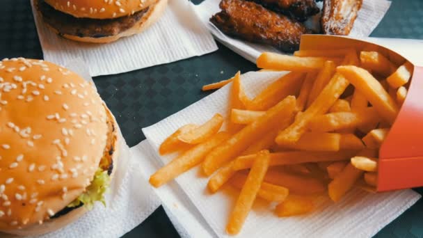 Na bandeja é fast food. Comida não saudável na mesa hambúrgueres, batatas fritas e asas de frango frito — Vídeo de Stock