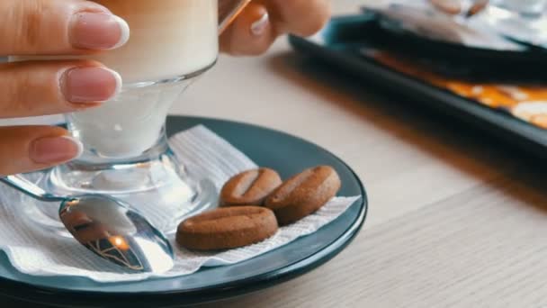 Skleněná kádinka s kávou, třídí od tmavě hnědé až mléčně bílá. Krásný latte s velkou pěnou v kavárně. Žena se dotýká skla s horké latte — Stock video