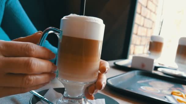 Cam kademeli koyu kahverengi sütlü beyaz renk ile kahve latte ile. Kafede büyük köpük ile güzel latte. Bir bardak latte ile tutan güzel eller — Stok video