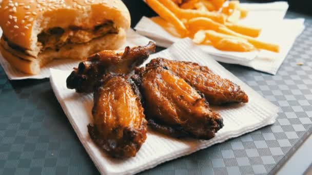 Mão das mulheres leva asas de frango frito, ao lado de uma bandeja encontra-se um hambúrguer picado e batatas fritas. Restaurante fast food — Vídeo de Stock