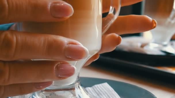 Becher in vetro con caffè, gradato dal marrone scuro al bianco latte. Bellissimo latte macchiato con una grande schiuma nel caffè. Una donna tocca un bicchiere con un latte caldo — Video Stock