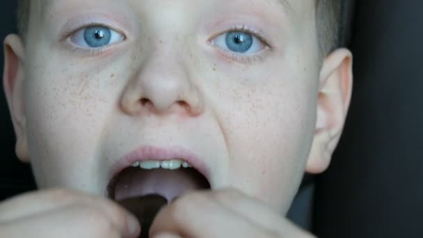 Szeplős szőke fiú tinédzser a kék szemével eszik csokoládé zár-megjelöl kilátás — Stock videók