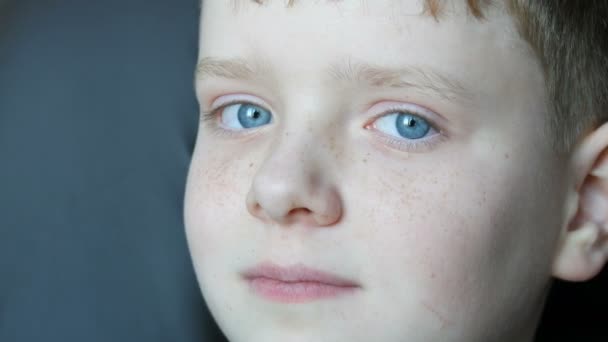 Μπλε μάτια έφηβος ξανθό αγόρι με κόκκινες φακίδες στο πρόσωπό του και μακριές άσπρες βλεφαρίδες που φαίνεται στην κάμερα — Αρχείο Βίντεο