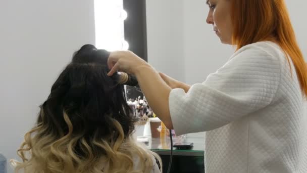 El peinado profesional hace rizos de rizos con la ayuda de una rizadora a una hermosa mujer joven con el pelo largo teñido utilizando la técnica ombre en el estudio de belleza — Vídeo de stock